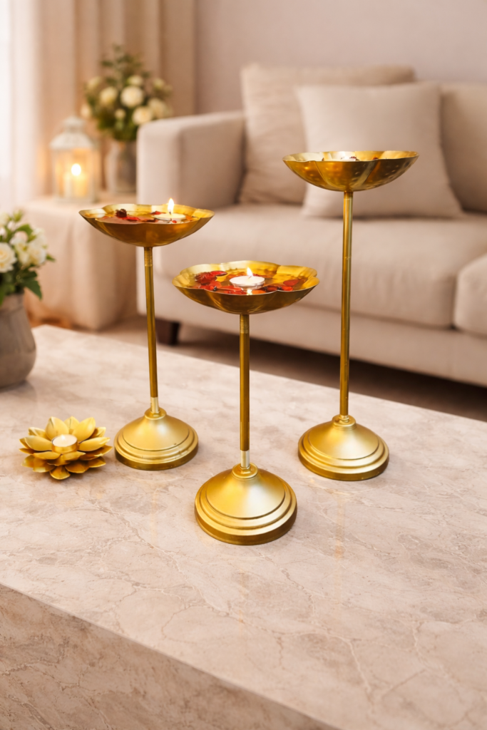 Set of three gold metal urli bowl tealight holders with stands, decorated with floating candles and flower petals for festive home decor.